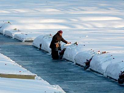 Mulher leva flores ao cemit�rio Piskaryovskoye coberto de neve, em S�o Petersburgo, onde hoje fez -21�C. Foto: AP