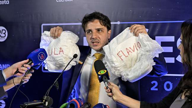 Renan Santos leva fraldas com nomes de Lula e Flávio Bolsonaro para debate na Band: ‘Dois medrosos’